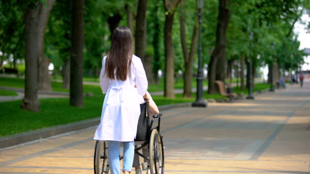 Weibliche-Krankenschwester-zu-Fuß-im-Park-mit-behinderten-Patienten,-Rehabilitationszentrum