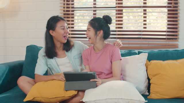 Young-Lesbian-lgbtq-Asian-women-couple-using-tablet--watching-movie-on-internet-together-while-lying-sofa-in-living-room.