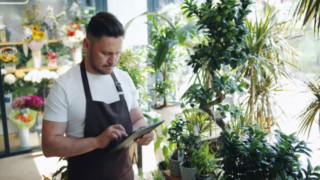 Slow-motion-of-man-flower-store-owner-using-tablet-at-work-touching-screen