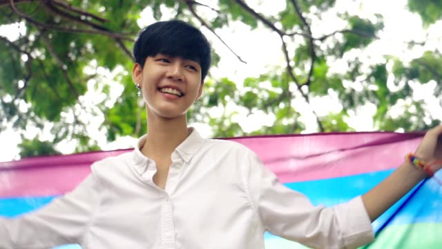 Glückliche-junge-asiatische-Tomboy-Mädchen-tanzen-und-winken-Regenbogen-LGBT-Flagge-im-Park,-Zeitlupe