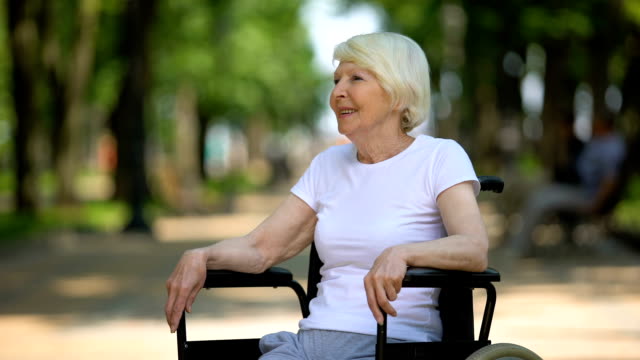 Happy-elderly-female-in-wheelchair-enjoying-sunny-day-in-park,-rehabilitation