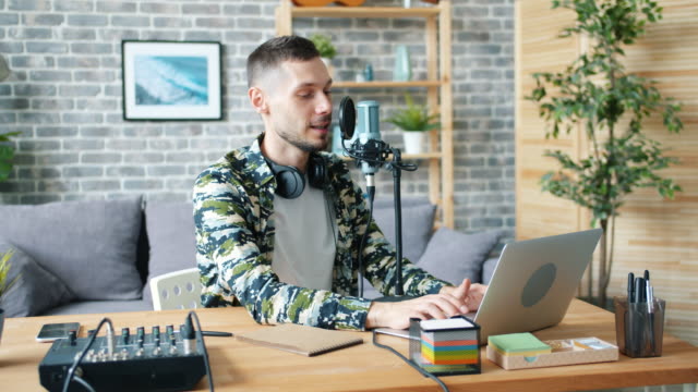 Guy-using-microphone-and-laptop-talking-recording-podcart-in-apartment