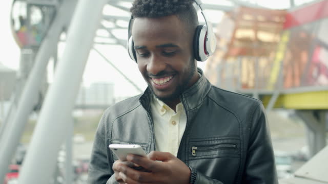 Slow-motion-of-African-American-man-using-smartphone-laughing-outdoors