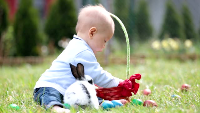 Dulce-niño-bebé-a-la-caza-de-huevos-de-pascua-en-el-parque-de-primavera-en-el-día-de-Pascua.-Lindo-niño-con-adorable-lindo-conejito-celebrando-fiesta-al-aire-libre
