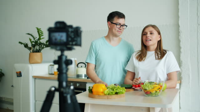 Chica-y-chico-grabando-video-sobre-comida-orgánica-con-cámara-en-la-cocina-en-casa