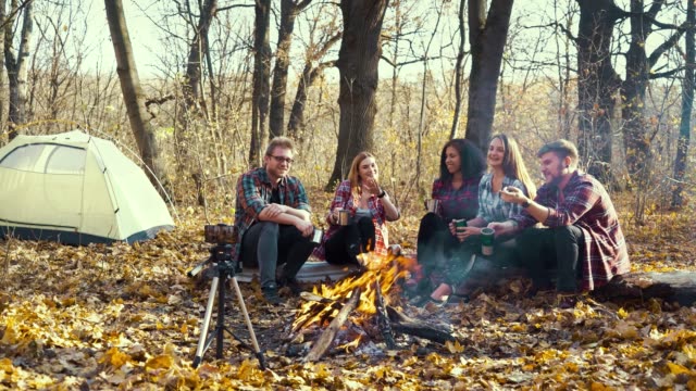 Travelers-sitting-by-campfire-and-live-streaming-using-smartphone-on-tripod