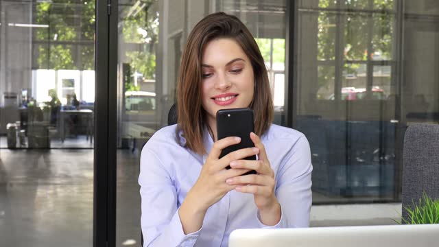 Funny-euphoric-young-woman-texting-message-on-smartphone-at-modern-office.-Excited-girl-receive-read-good-news-on-cellphone.