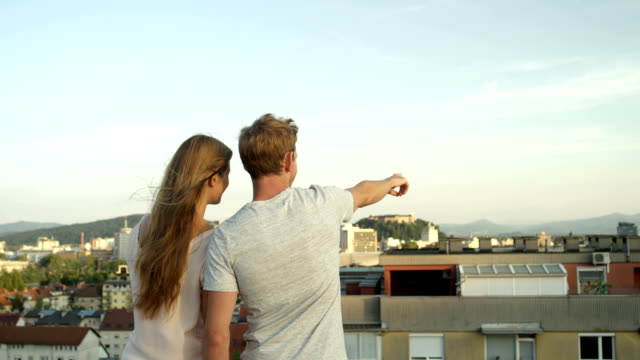 CLOSE-UP:-Lovers-standing-on-rooftop-looking-on-stunning-city-pointing-fingers