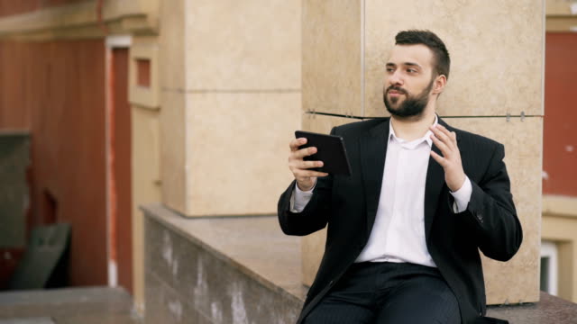 Young-bearded-business-man-talking-on-tablet-computer-having-video-chat-business-meeting.-Businessman-using-app-to-have-video-conference-conversation