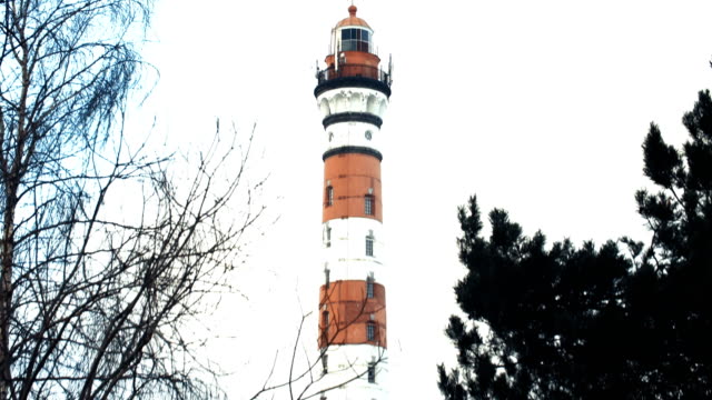 Red-and-white-lighthouse,-in-winter-the-trees-in-the-foreground
