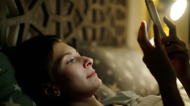 Nahaufnahme-der-junge-lächelnde-Frau-mit-Smartphone-liegend-im-Bett-zu-Hause-in-der-Nacht