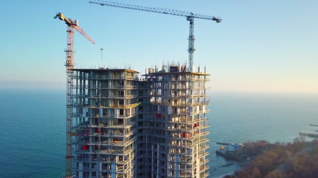 Aerial-city-view.-Construction-of-a-high-rise-skyscraper-on-the-ocean-by-two-cranes.-Even-slow-travel