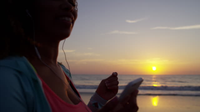 Afroamerikanische-Frau-mit-Kopfhörern-bei-Sonnenaufgang-tanzen
