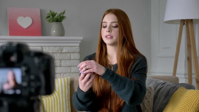 Young-red-haired-girl-blogger,-smiling,-talking-at-the-camera,-showing-a-new-purchase,-cosmetics,-rouge,-blush,-powder,-make-up-concept,-home-comfort-in-the-background.-60-fps