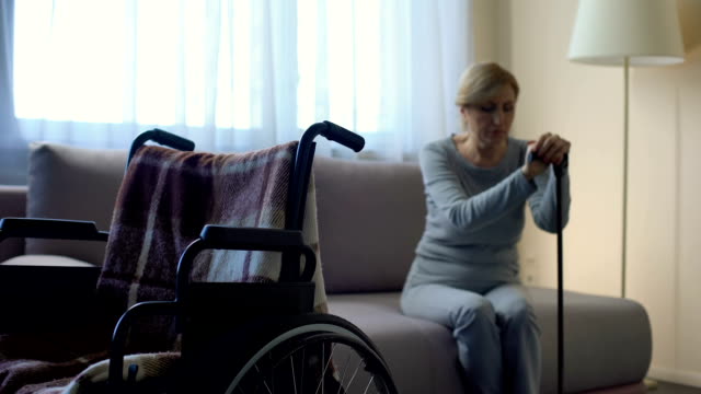 Einsame-behinderte-Frau-auf-Sofa-sitzen-und-mit-Blick-auf-leeren-Rollstuhl,-Erinnerungen