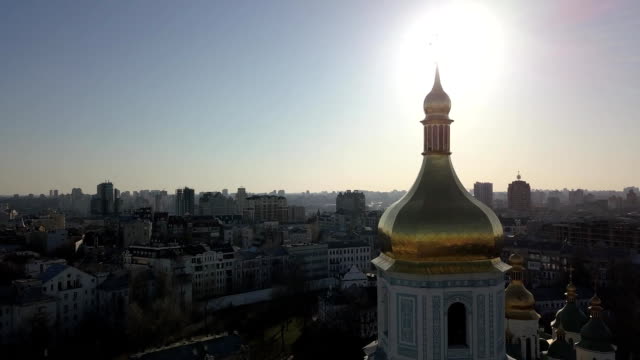 Ve-el-ojo-de-un-pájaro,-video-panorámico-desde-el-drone-en-FullHD-a-la-cúpula-dorada-de-la-campana-de-torre-de-Santa-Sofía-de-Catedral-en-la-ciudad-de-Kiev,-Ucrania-contra-un-sol-brillante.
