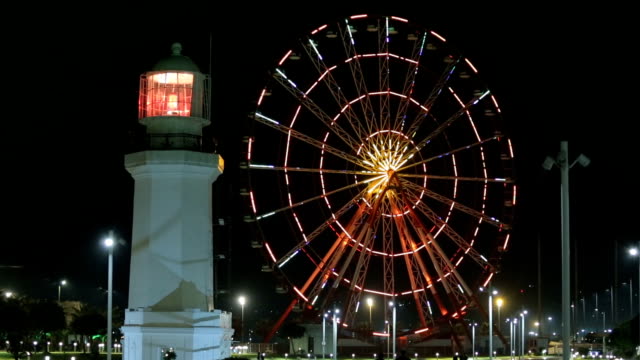 Illuminated-ferris-wheel-and-lighthouse,-Batumi-landmark-architecture,-tourism