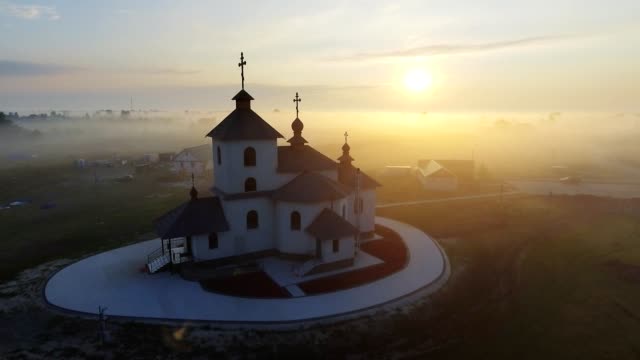 Aerial-footage-video-of-small-village-church-at-the-foggy-morning.-Sunrise-time.-Kyiv-region,-Ukraine.-Flying-over-the-Desna-river