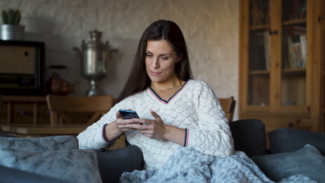woman-sitting-on-the-couch-wrapped-in-a-blanket-and-texting-on-the-phone