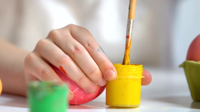 Children-hands-preparing-yellow-paint-to-draw-pattern-on-egg,-Easter-preparation