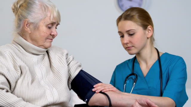 Junge-Krankenschwester-messen-behinderte-ältere-weibliche-Blutdruck-und-Einnahme-Datensätze