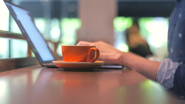 Händen-eines-Mannes,-männliche-digital-Nomad-schreiben,-tippen-auf-Laptop,-online-arbeiten-und-trinken-Kaffee-aus-einem-orange-Cup-in-einem-Coffee-Shop,-Tiefe-erschossen