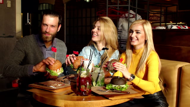 Amigos-felices-están-comiendo-hamburguesas,-hablando-y-sonriendo-en-un-café.