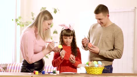 familia-con-hija,-casa-decorar-huevos-de-Pascua-en-la-mesa-son-de-pintura-y-una-cesta-de-huevos.