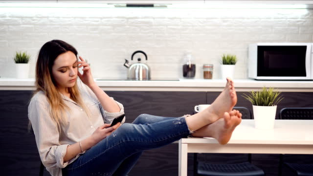 Young-girl-is-sitting-in-spacious-bright-kitchen-using-smartphone.