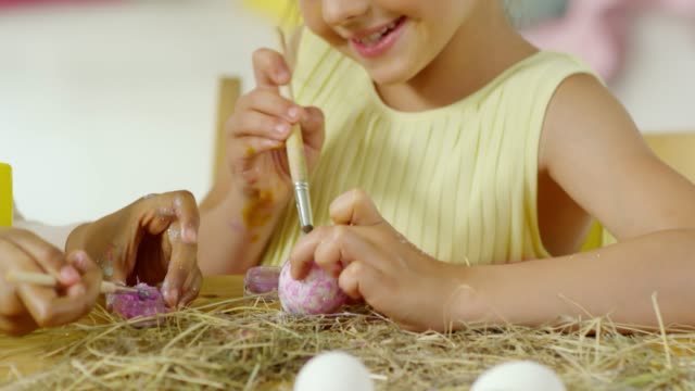 Linda-niñita-sonriendo-y-poniendo-brillo-en-huevo-de-Pascua