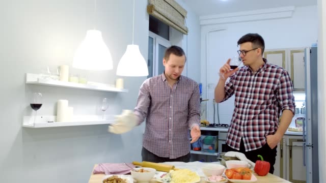 Couple-of-men-gay-flirts-each-other-cooking-a-pizza-together-and-drinking-a-wine.
