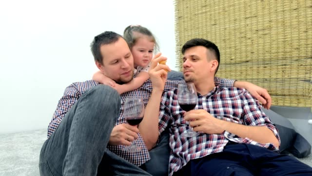 Schwule-Familie-mit-Tochter-essen-Mandarine-und-trinken-gemeinsam-Wein-im-Wohnzimmer.