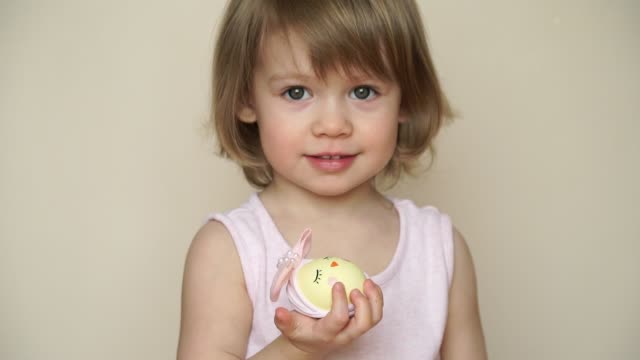Porträt-des-kleinen-ziemlich-lächelnden-kaukasischen-Mädchens-hält-Hühnerei-für-Osterschick-dekoriert,-mit-bemalten-Schnauze-mit-Augen-und-Bogen.