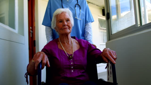 Vista-frontal-de-mujer-caucásica-médico-empujando-paciente-Senior-en-silla-de-ruedas-en-casa-de-ancianos-4k