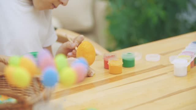 El-niño-intersted-y-concentrado-está-terminando-de-colorear-un-huevo-de-Pascua-en-un-color-amarillo,-sentado-en-el-escritorio.