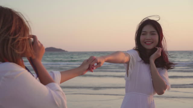 Young-Asian-lesbian-couple-using-camera-taking-photo-each-other-near-beach.-Beautiful-women-lgbt-couple-happy-romantic-moment-when-sunset-in-evening.-Lifestyle-lesbian-couple-travel-on-beach-concept.