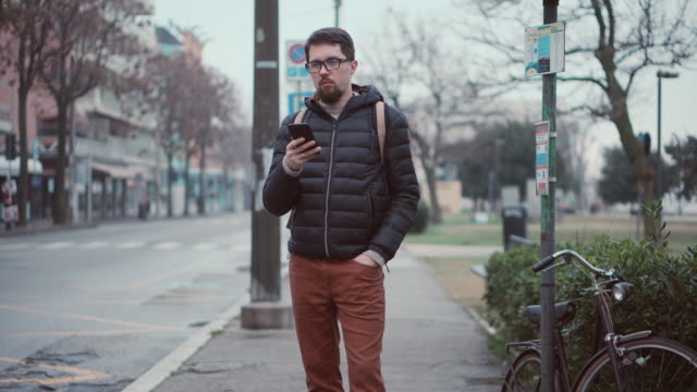 Man-is-waiting-bus-on-station-and-using-smartphone