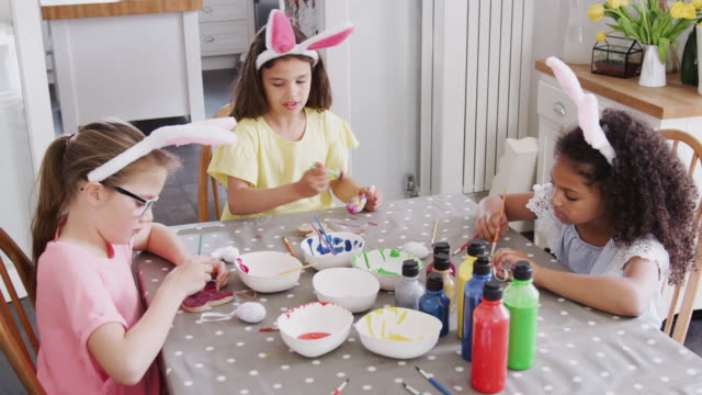 Gruppe-von-Mädchen-sitzen-um-Küchentisch-mit-Hasenohren-schmücken-Eier-für-Ostern---in-Zeitlupe-geschossen