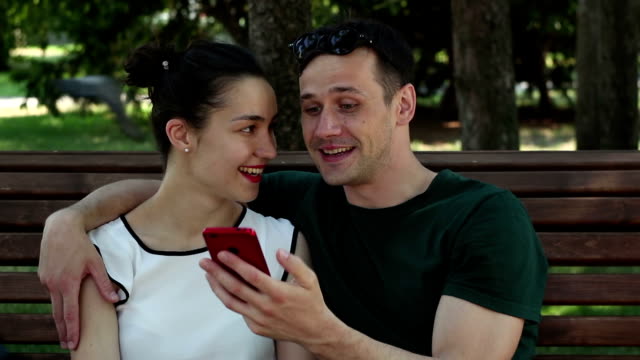 Young-couple-in-love-is-photographed-sitting-on-a-bench-in-the-park.They-are-smiling-and-hugging-each-other.