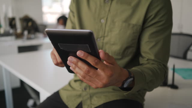 Primer-plano-de-un-joven-empresario-con-camisa-sentado-en-el-escritorio-blanco-usando-tableta-digital-en-la-oficina-moderna