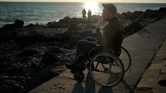 Männlicher-Rollstuhlfahrer-schaut-aufs-Meer-und-denkt-im-Frühling-abend