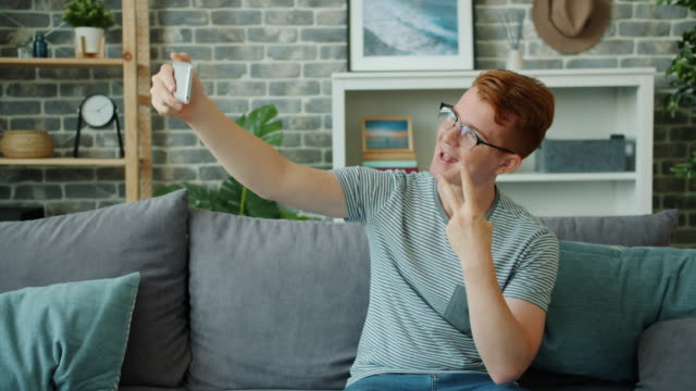 Fröhlicher-Teenager-macht-Selfie-mit-Smartphone-Kamera-posiert-auf-der-Couch-zu-Hause