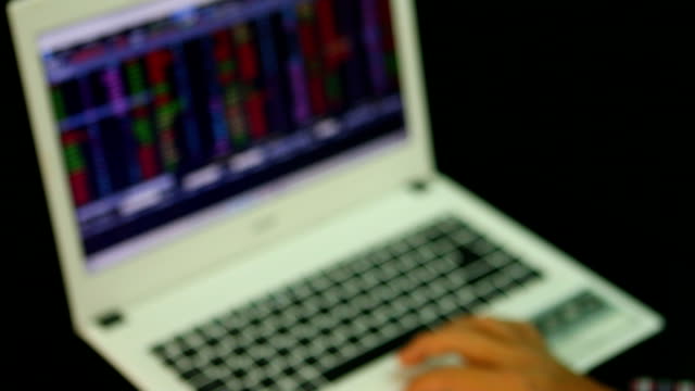Blurred-man--using-notebook-monitoring--stock-exchange-board