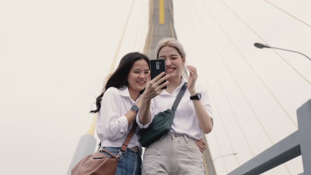 Happy-Asian-lesbian-couples-selfie-video-chat-with-friends-enjoying-traveling-in-Thailand.-Beautiful-young-women-having-fun-in-vacation-time.-LGBT-concept.