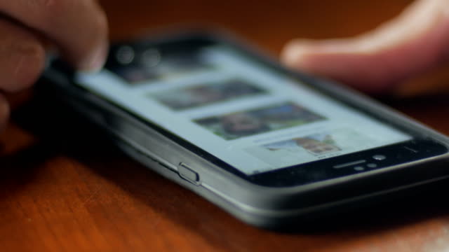 Closeup-of-man-scrolling-through-smart-phone-photos-on-desk