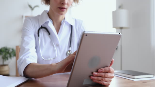 Primer-plano-de-la-doctora-que-usa-la-aplicación-de-tableta-digital-en-el-lugar-de-trabajo