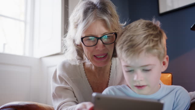 Nahaufnahme-von-Enkel-mit-Großmutter-sitzt-im-Stuhl-spielen-auf-digitalen-Tablet-zu-Hause-zusammen