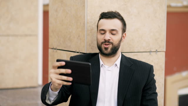 Young-businessman-talking-on-tablet-computer-having-video-chat-with-his-wife.-Business-man-using-app-to-have-video-conference-conversation-with-his-family-during-break