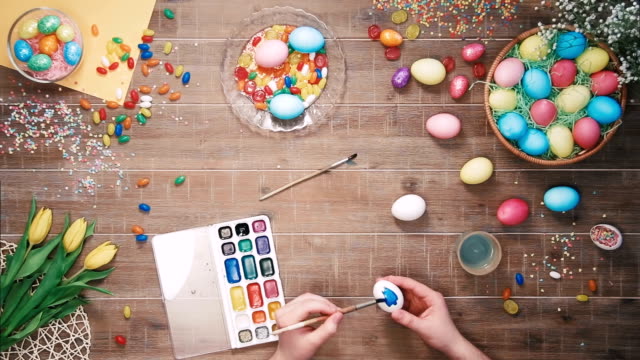 Man's-hands-painting-easter-eggs-on-table-decorated-with-easter-eggs.-Top-view
