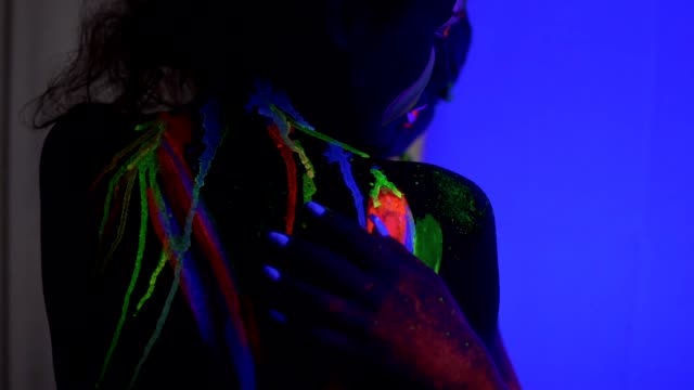Closeup-view-of-two-beautiful-girls-with-fluorescent-makeup-and-body-art-under-UV-black-light-petting-each-other-and-hugging.-Slowmotion-shot